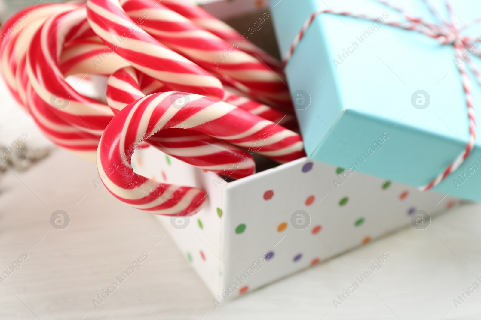 Photo of Many sweet candy canes in gift box on white wooden table, closeup. Traditional Christmas treat