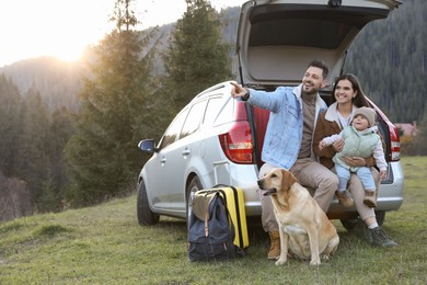 Parents, their daughter and dog near car in mountains, space for text. Family traveling with pet