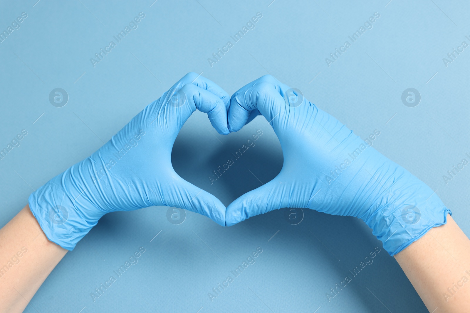 Photo of Doctor showing heart gesture with hands on light blue background, top view