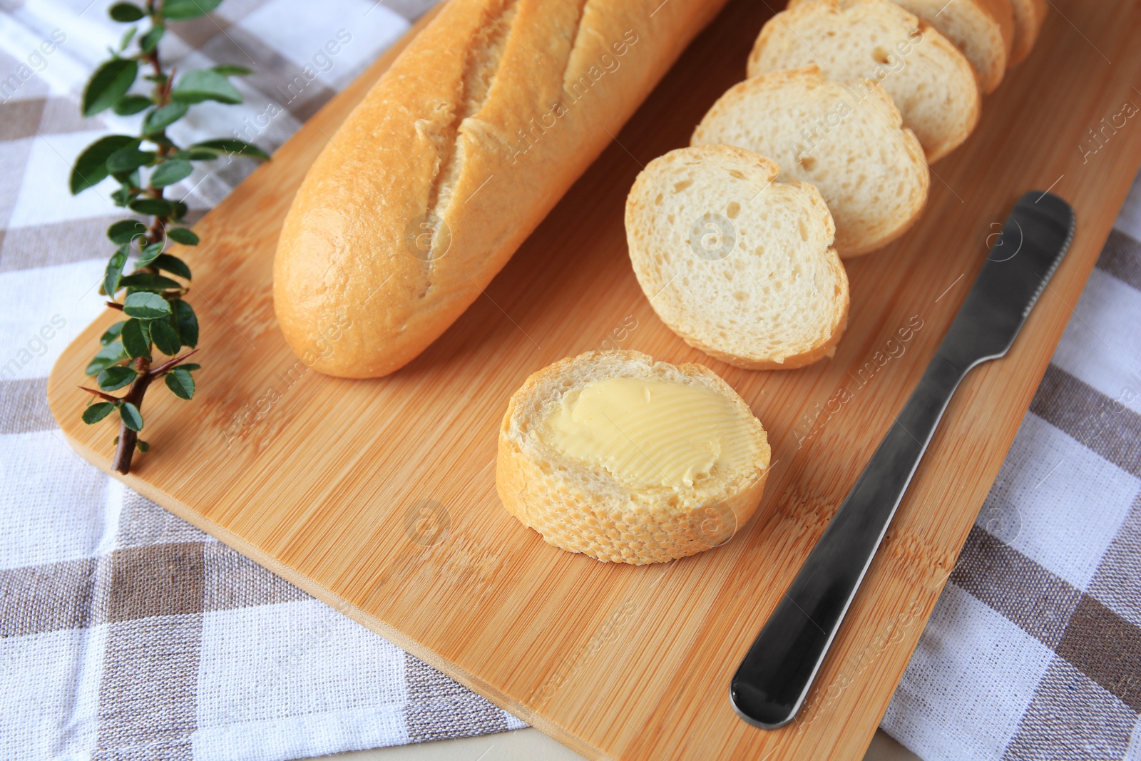 Photo of Cut baguette with fresh butter on checkered tablecloth, closeup