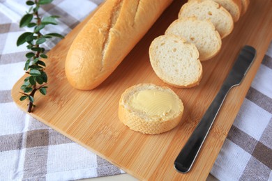 Photo of Cut baguette with fresh butter on checkered tablecloth, closeup