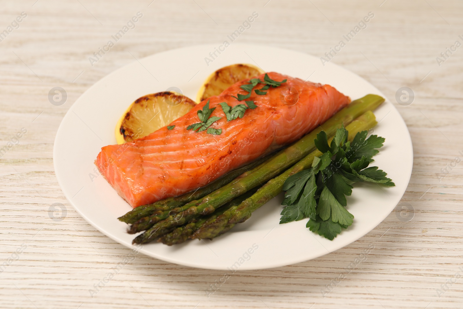 Photo of Tasty grilled salmon with asparagus and lemon on white wooden table, closeup