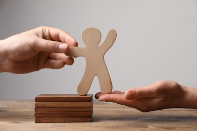 Women holding human figure at wooden table, closeup