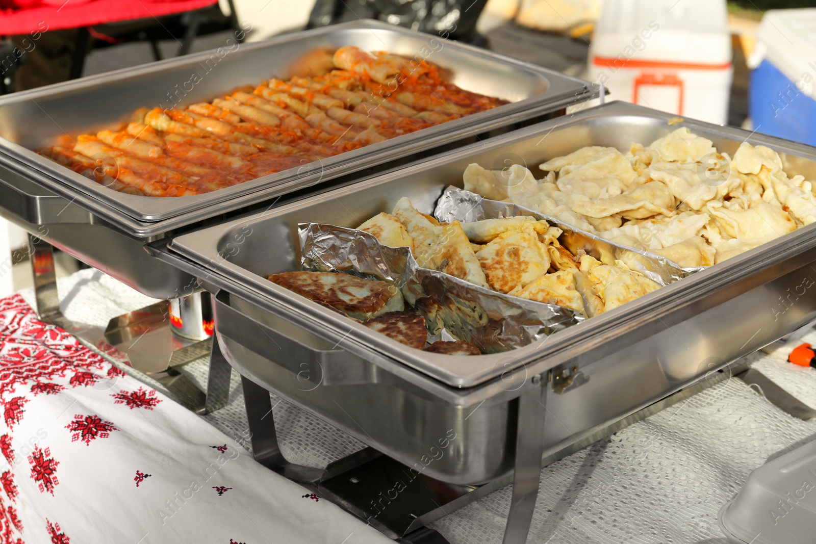 Photo of Delicious stuffed cabbage, dumplings and patties in warmers on table outdoors. Volunteer food distribution