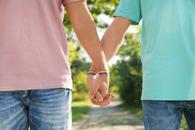 Photo of Gay couple with wristbands holding hands outdoors, closeup