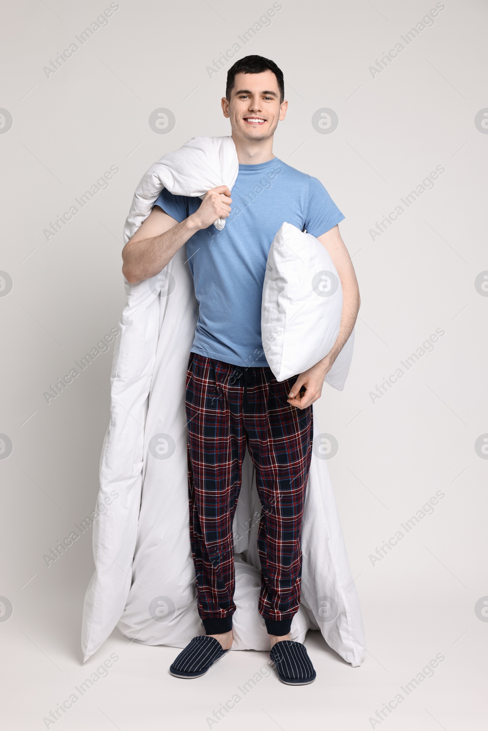 Photo of Happy man in pyjama with blanket and pillow on light grey background
