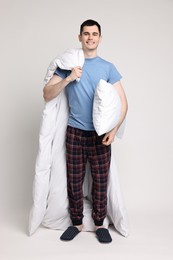 Happy man in pyjama with blanket and pillow on light grey background