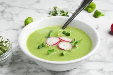 Photo of Bowl of broccoli cream soup with radish and microgreens served on white marble table