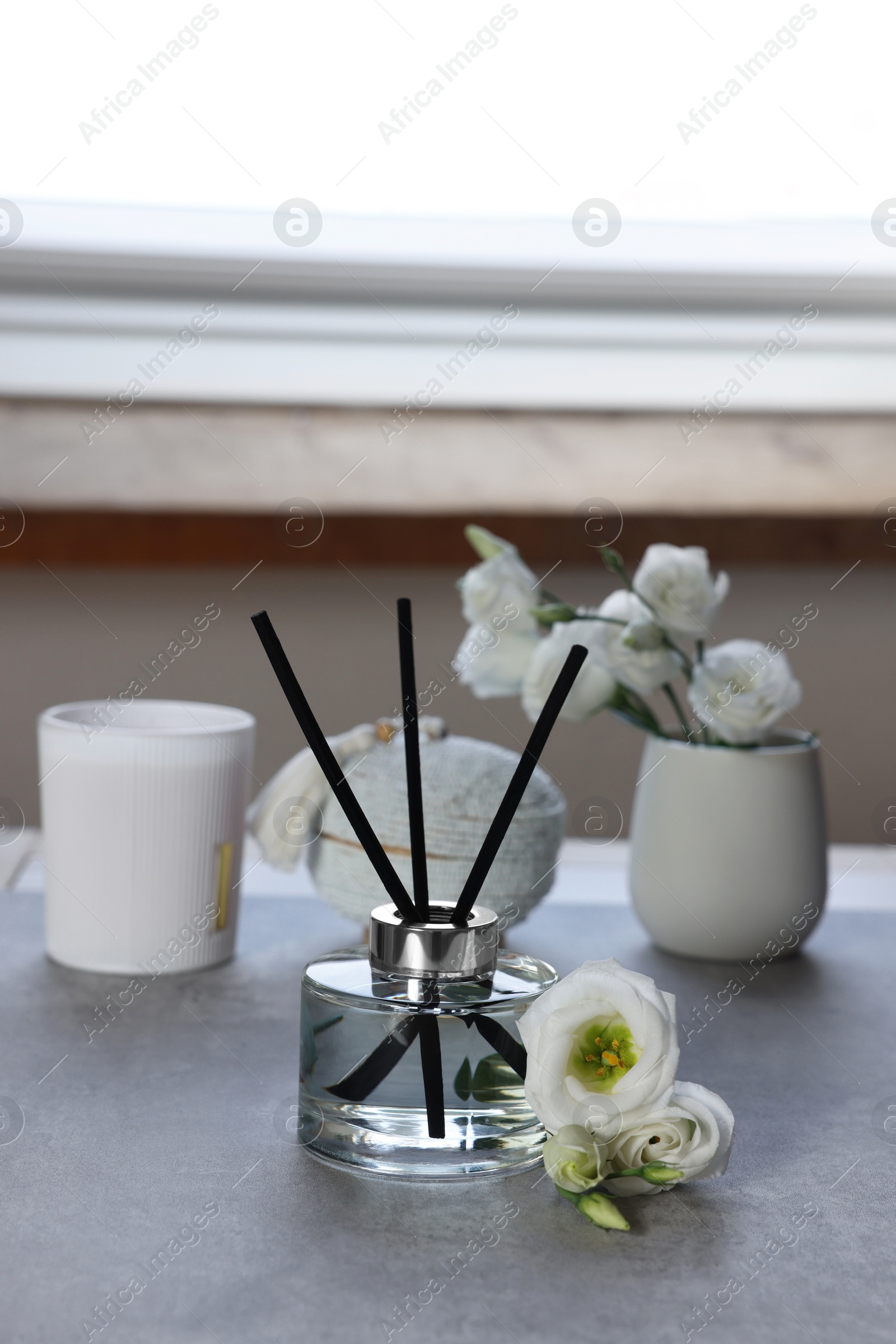 Photo of Reed diffuser, scented candle and eustoma flowers on gray marble table