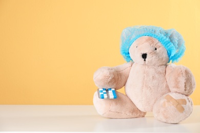 Photo of Toy bear with pills on table against color background, space for text. Children's hospital