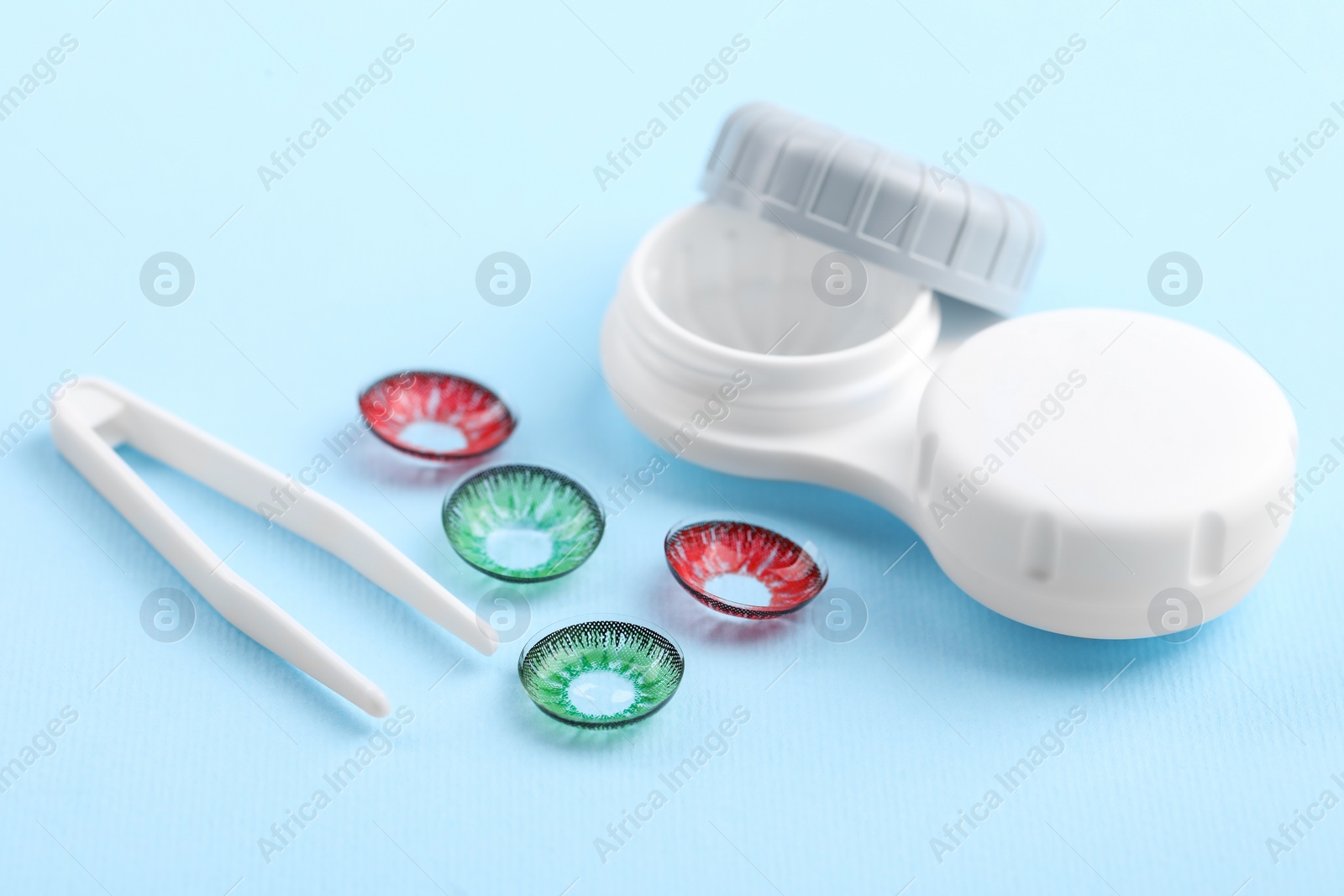 Photo of Different color contact lenses, case and tweezers on light blue background