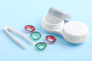 Photo of Different color contact lenses, case and tweezers on light blue background
