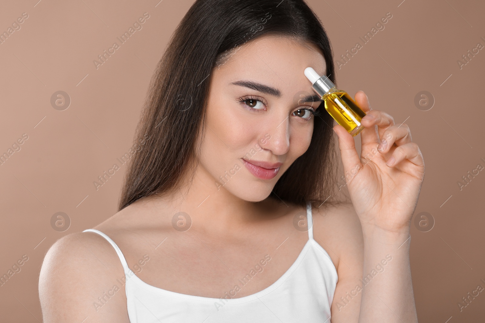 Photo of Beautiful young woman with bottle of essential oil on brown background