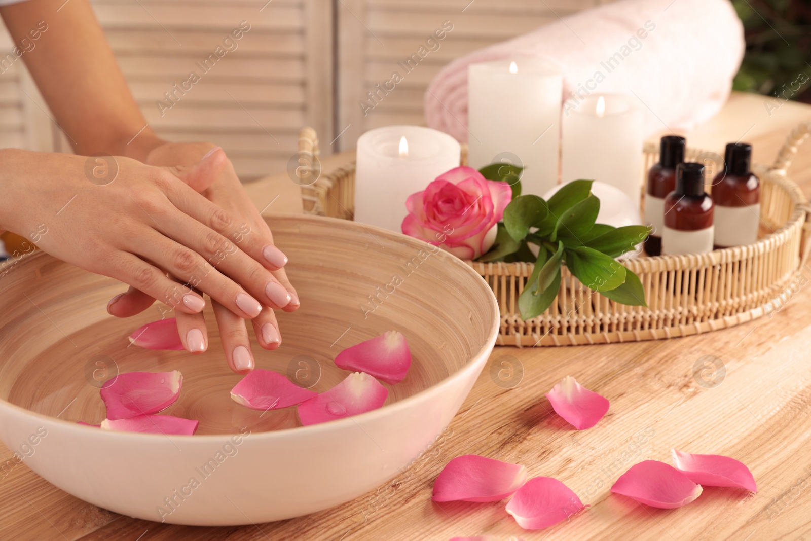 Photo of Woman soaking her hands in bowl of water and petals on table, closeup with space for text. Spa treatment