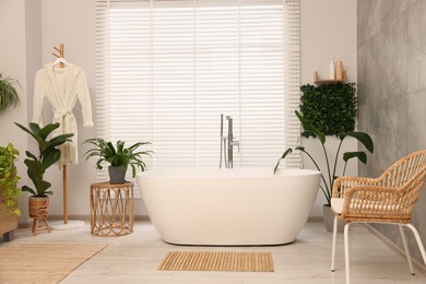Photo of Green artificial plants, robe and tub in bathroom