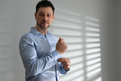 Man wearing stylish shirt and cufflinks near white wall, space for text