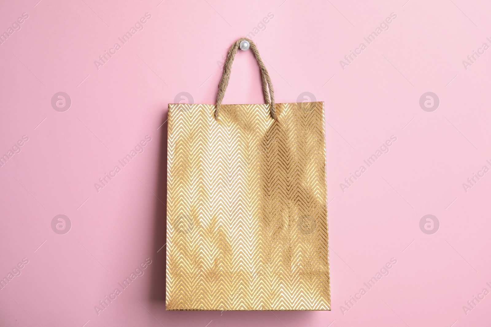 Photo of Gold shopping paper bag on pink background