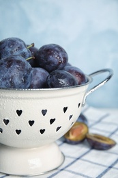 Delicious ripe plums in colander on table against light background