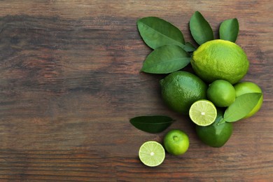 Photo of Whole and cut fresh ripe limes with green leaves on wooden table, flat lay. Space for text