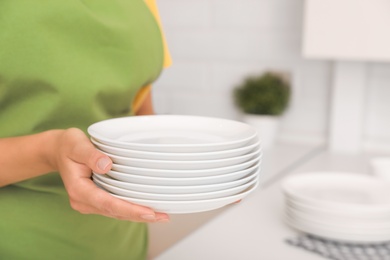Photo of Woman holding stack of clean dishes in kitchen, closeup. Space for text