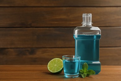 Photo of Mouthwash, mint and lime on wooden table, space for text