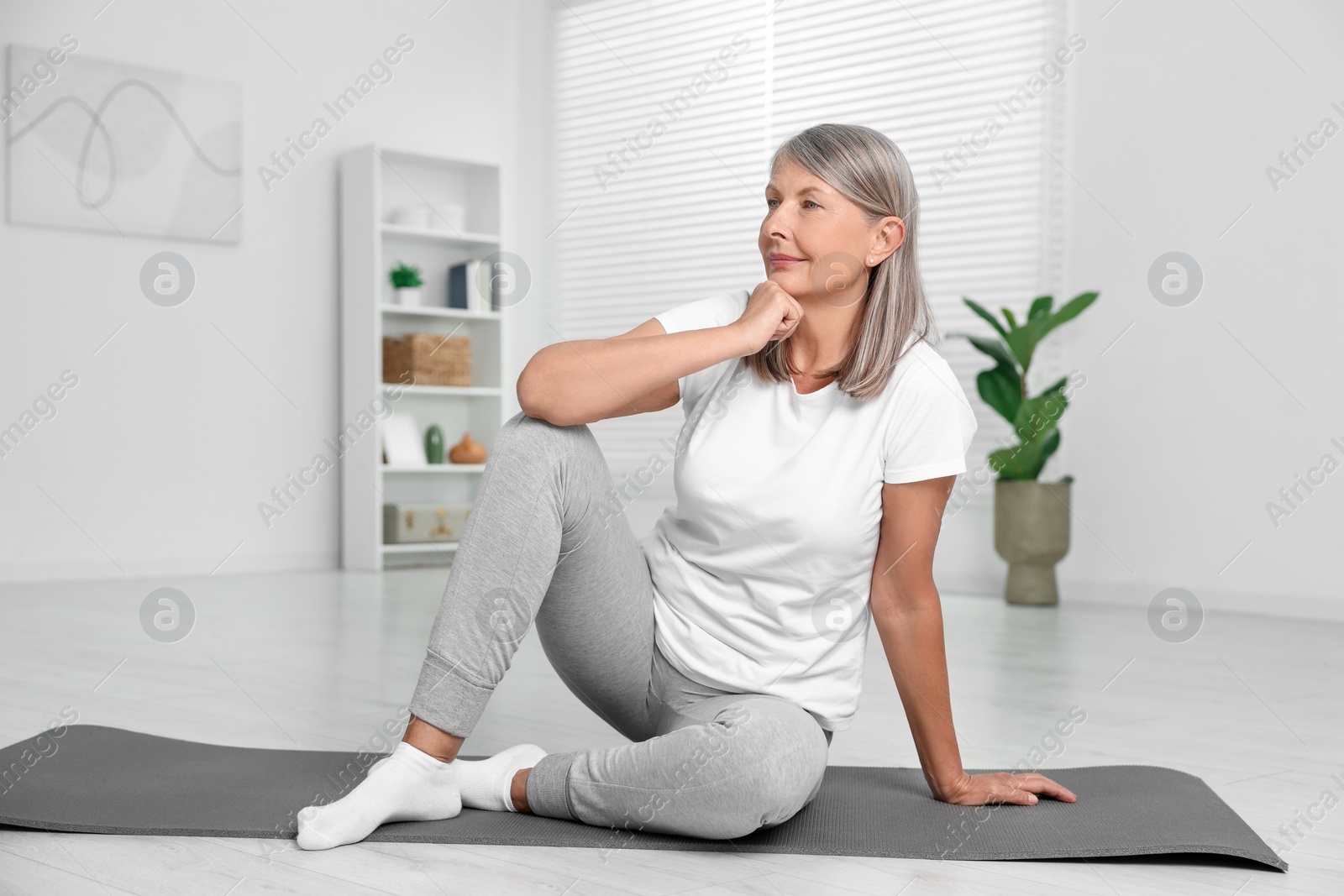 Photo of Senior woman sitting on mat at home. Yoga practice