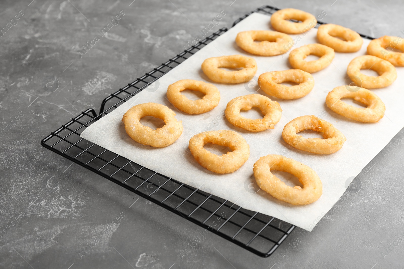 Photo of Cooling rack with tasty onion rings on gray table