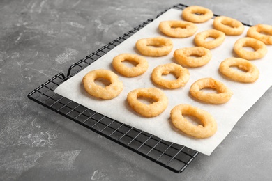 Photo of Cooling rack with tasty onion rings on gray table