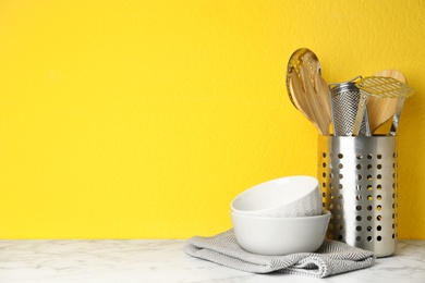 Photo of Different kitchen utensils on marble table against yellow background. Space for text