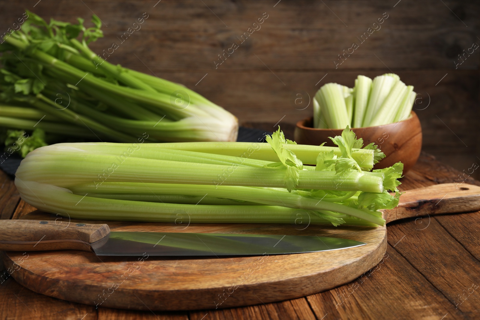 Photo of Fresh green celery bunches and knife on wooden table