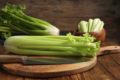 Photo of Fresh green celery bunches and knife on wooden table