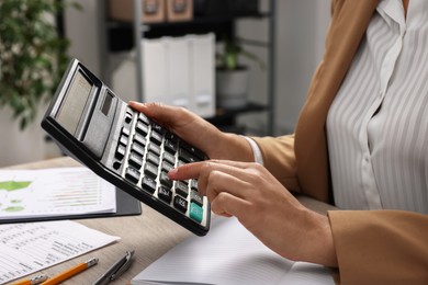 Photo of Woman using calculator at table in office, closeup