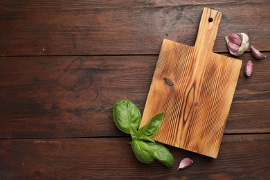 Photo of Cutting board, basil and garlic on wooden table, flat lay. Space for text