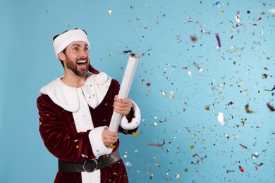 Photo of Emotional man in Santa Claus costume blowing up party popper on light blue background