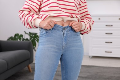 Photo of Woman trying to fit into her jeans at home, closeup