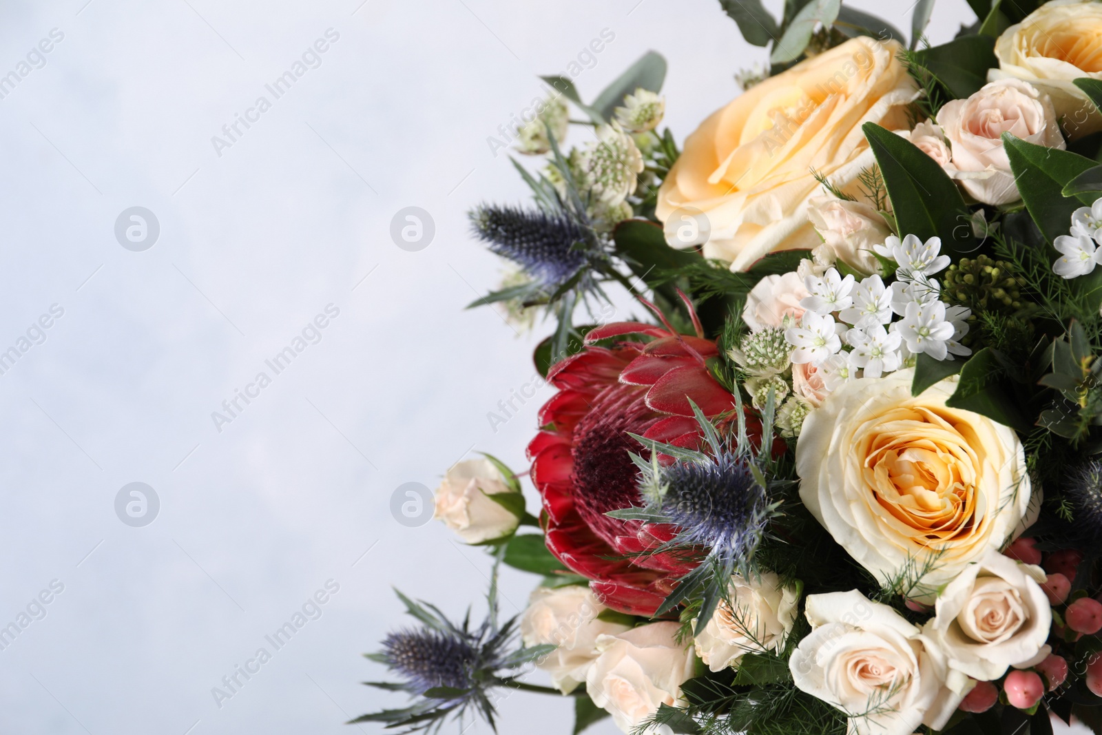 Photo of Beautiful bouquet with roses on light blue background, closeup. Space for text