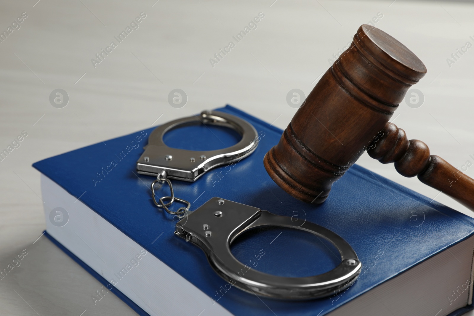 Photo of Judge's gavel, handcuffs and book on white wooden background, closeup. Criminal law concept