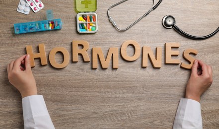 Doctor making word HORMONES with wooden letters at table, top view