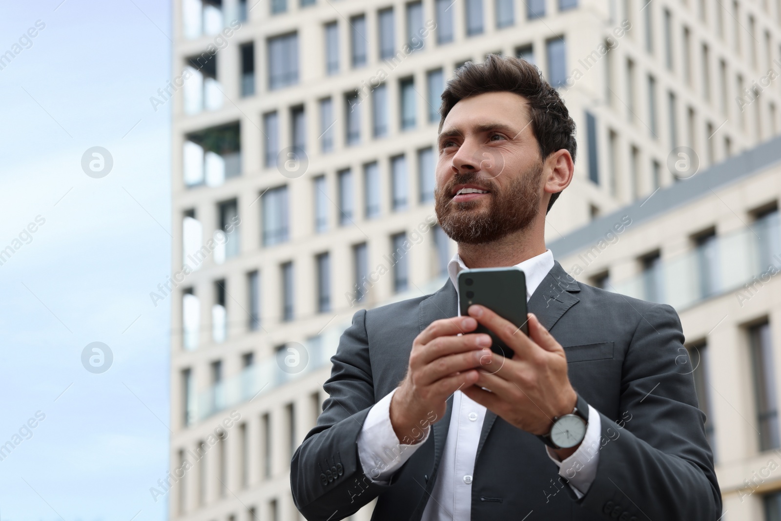 Photo of Handsome businessman with smartphone near buildings, space for text