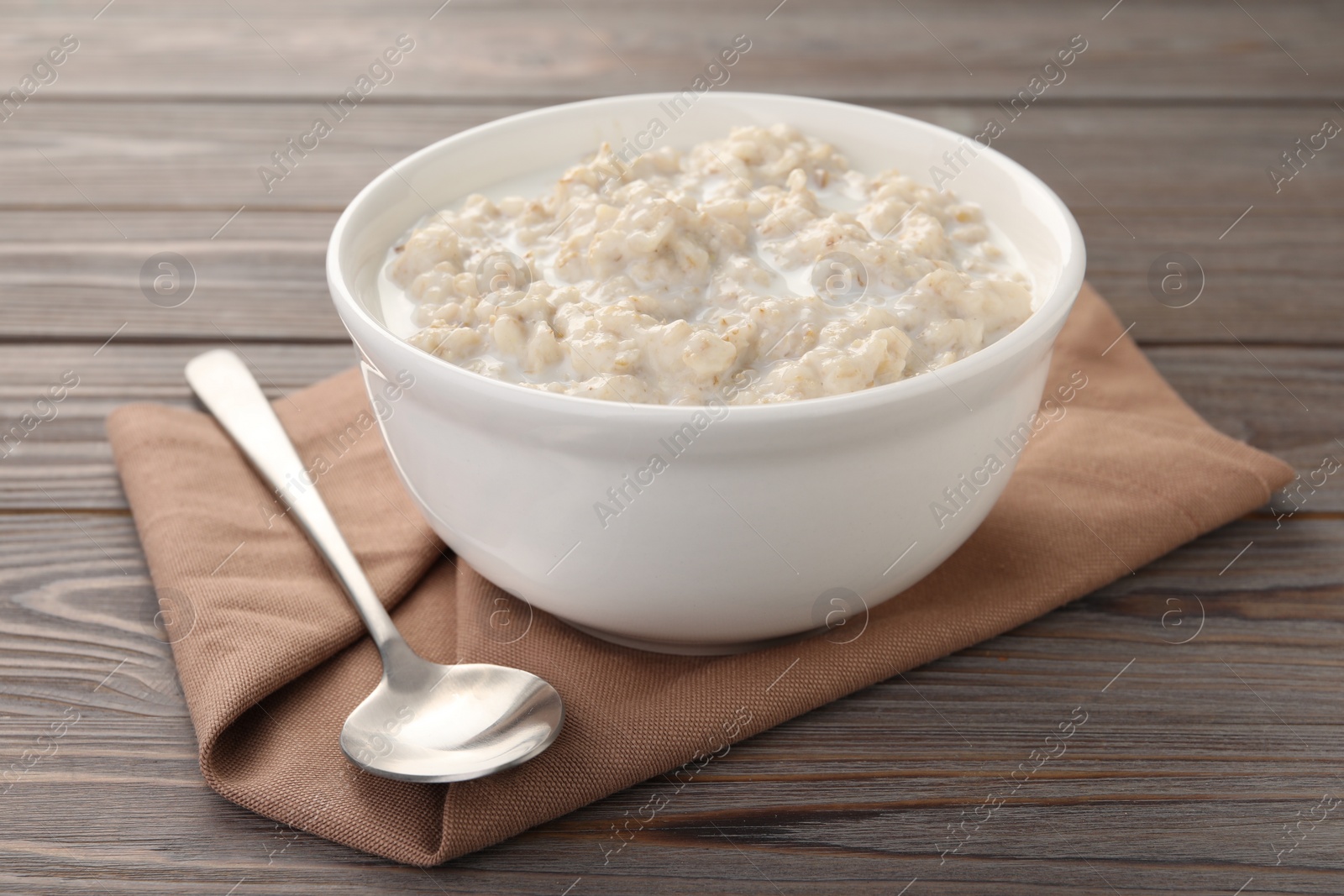 Photo of Tasty boiled oatmeal in bowl and spoon on wooden table, closeup