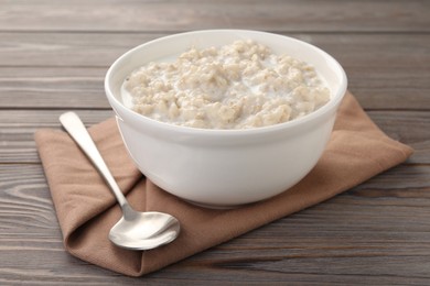 Photo of Tasty boiled oatmeal in bowl and spoon on wooden table, closeup