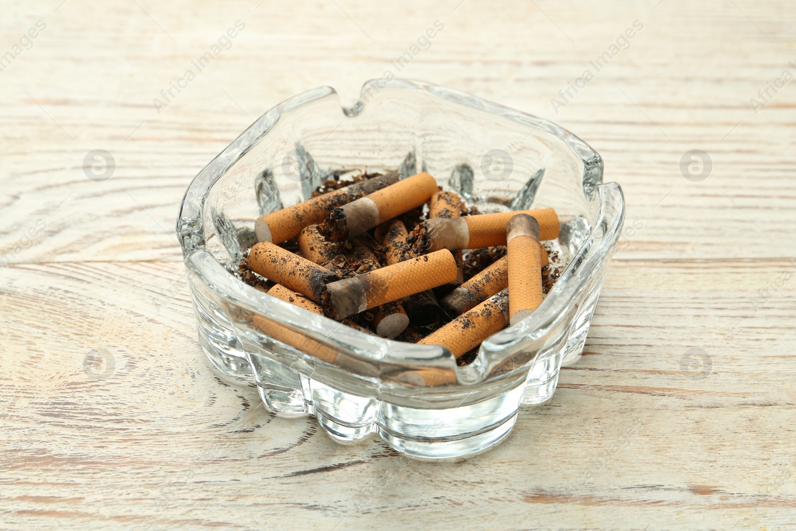 Photo of Glass ashtray with cigarette stubs on white wooden table