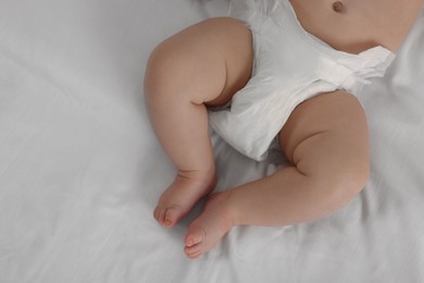 Photo of Little baby in diaper lying on bed, top view