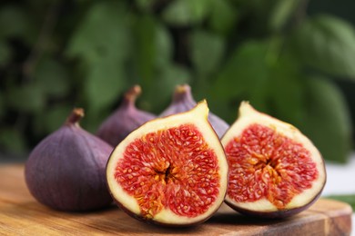 Photo of Tasty ripe figs on wooden board against blurred background, closeup