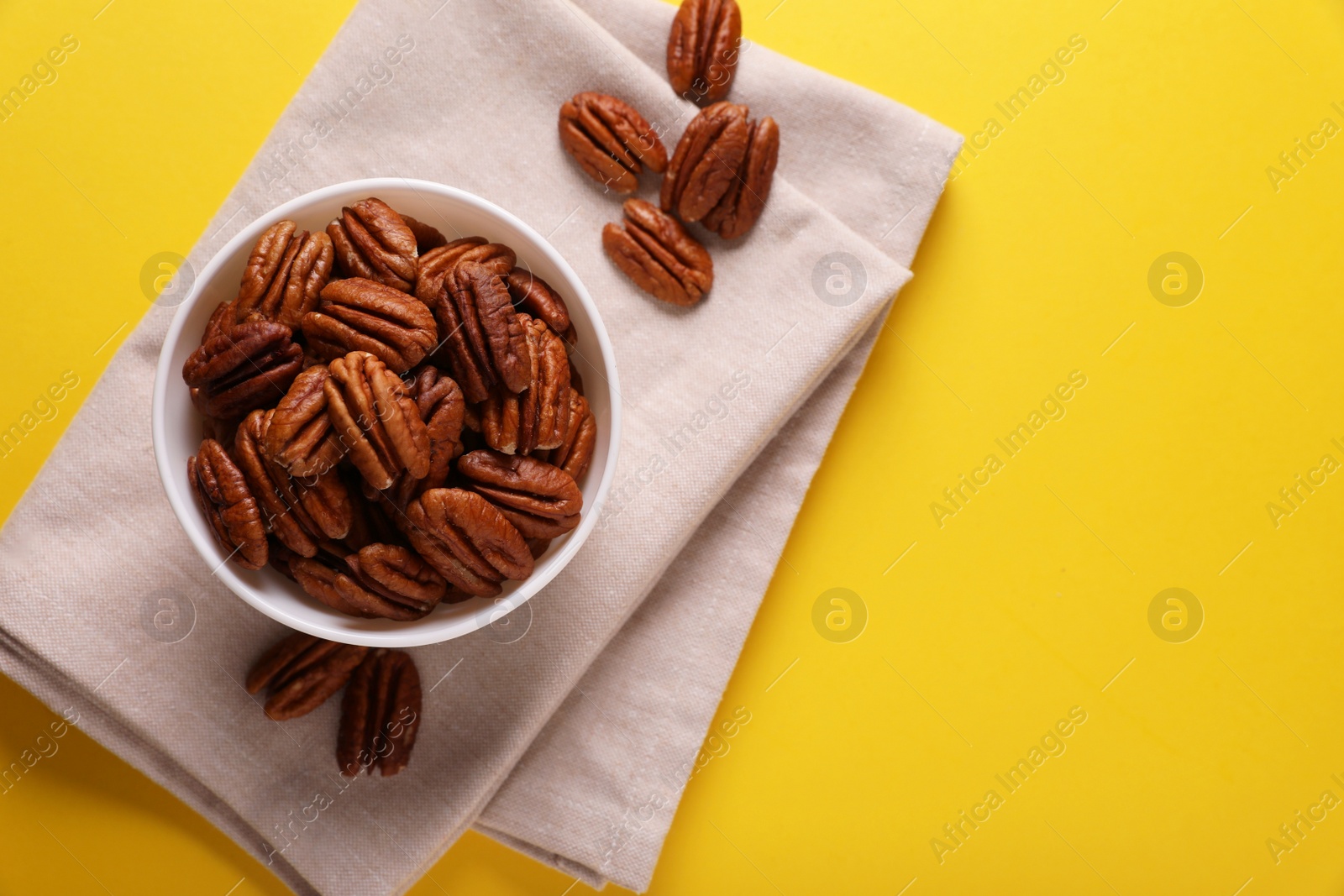 Photo of Bowl with tasty nuts on yellow background, flat lay. Space for text