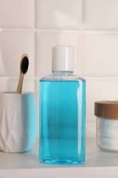 Photo of Bottle of mouthwash, toothbrush and cotton pads on white shelf in bathroom