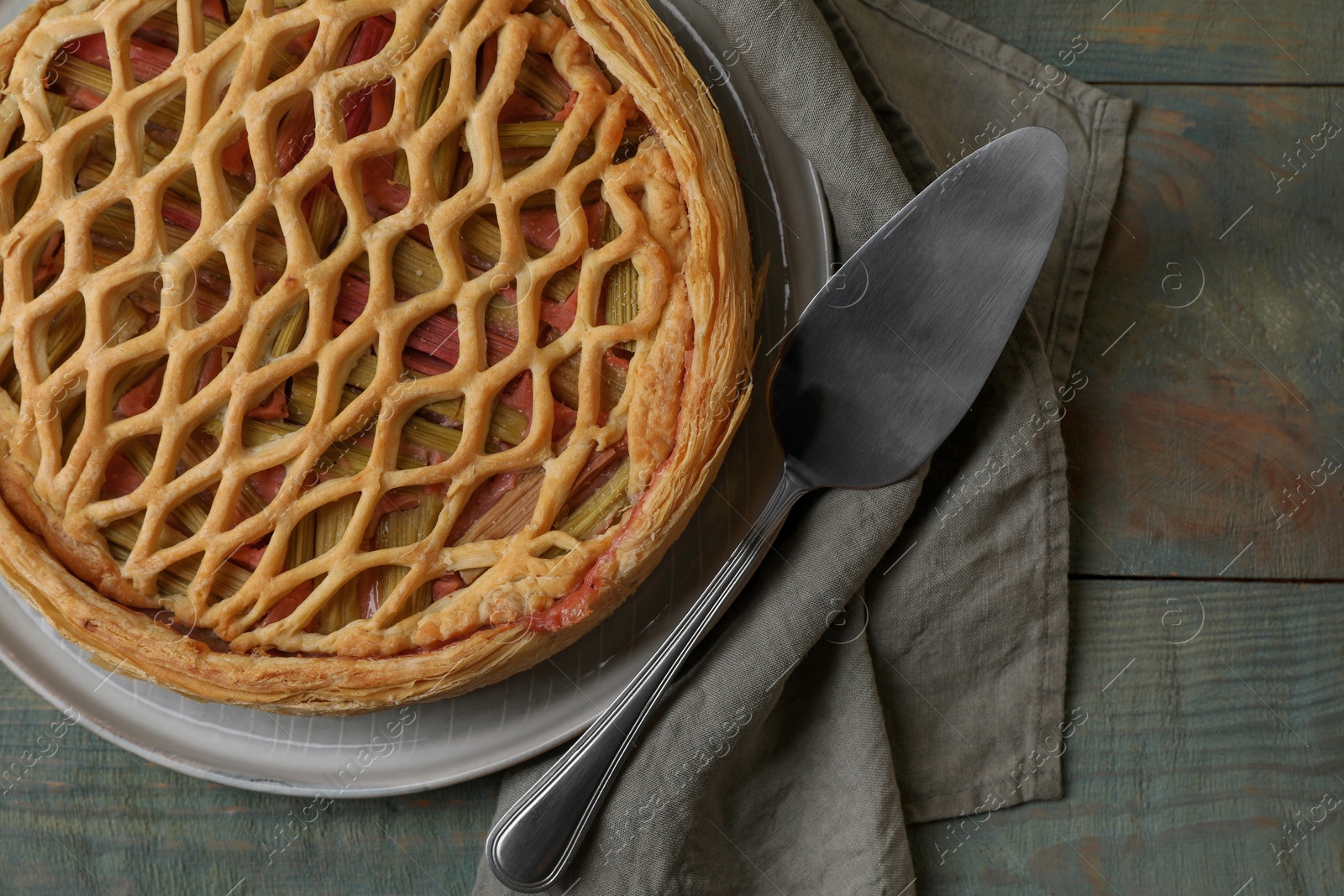 Photo of Freshly baked rhubarb pie and cake server on wooden table, flat lay