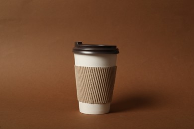 Takeaway paper coffee cup with cardboard sleeve on brown background