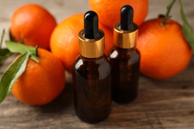 Photo of Bottles of tangerine essential oil and fresh fruits on wooden table, closeup