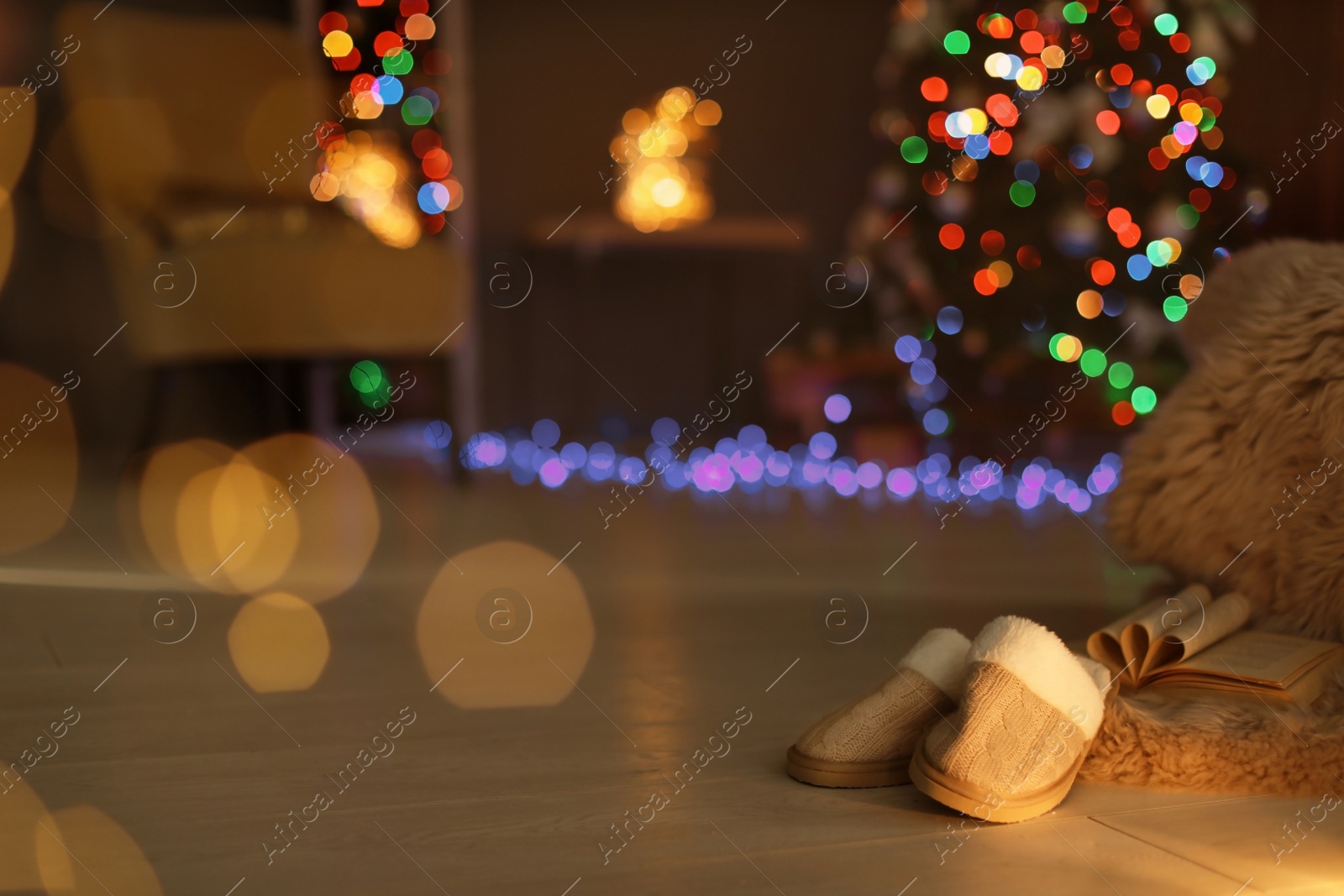 Photo of Soft slippers with fluffy blanket and Christmas tree in dark room